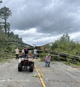 four men looking at a fallen tree acroos a two line hwy with atv and man kneeling at front of photo